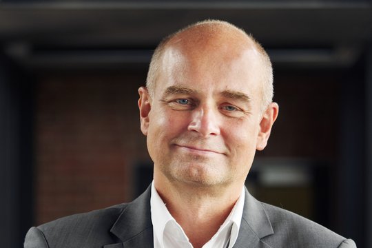 Prof. Dr Jürgen May: a researcher who is bald and wears a white shirt with a grey jacket.