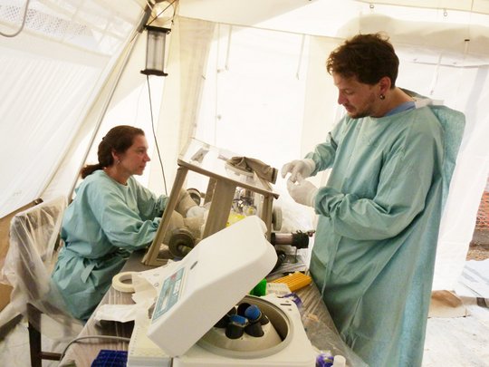 Das Bild zeigt Forscher an einer Glovebox in grüner Laborkleidung