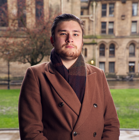 A man dressed in brown, buildings in the background