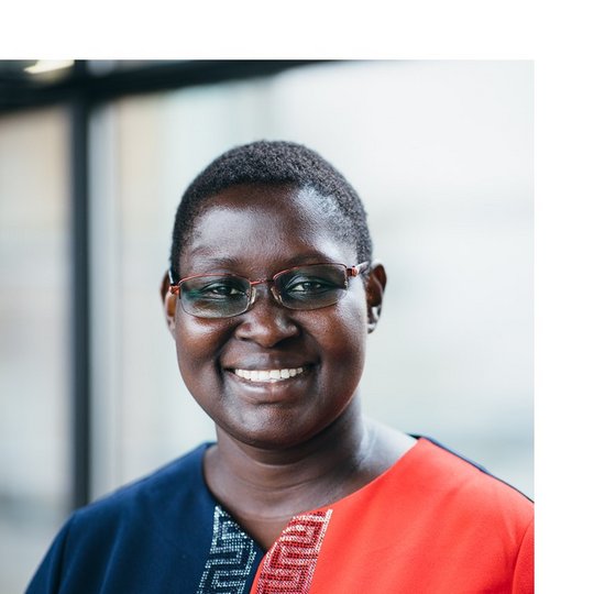 Portrait of a Black female person with glasses, wearing a blue and red dress.