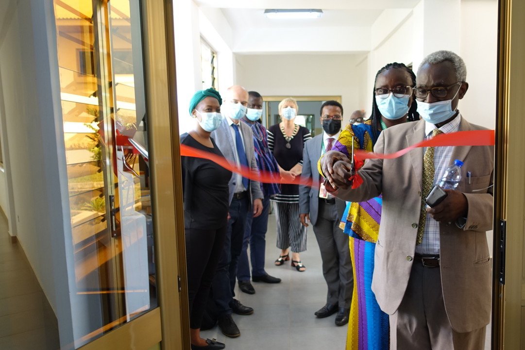 The picture shows the inauguration of the entomology wing of the KCCR. A woman and a man cut the red ribbon to the laboratory together. Behind them is a group of African and European people.
