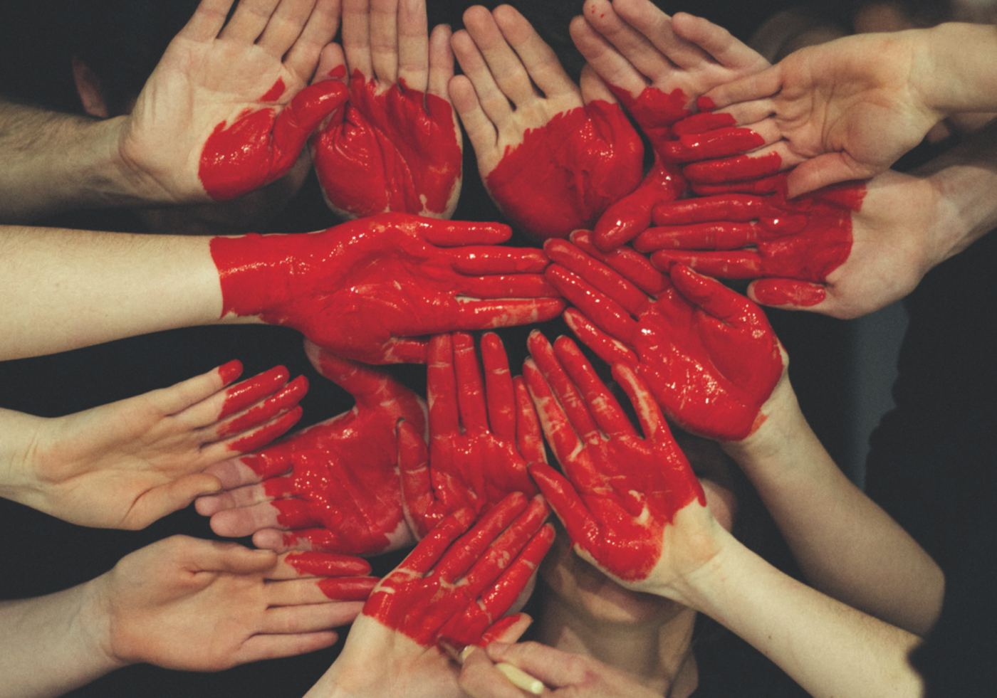 Several red painted hands together form a heart.