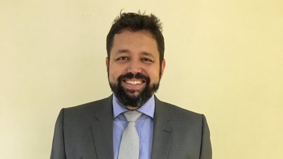 Dr. Rafael Maciel-de-Freitas: ein Forscher mit schwarzen haaren und schwarzem bart, trägt ein hellblaues Hemd, grauen Anzug und Krawatte.