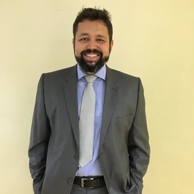 Dr Rafael Maciel-de-Freitas: a researcher with black hair and beard, wearing a light blue shirt, gray suit and tie.