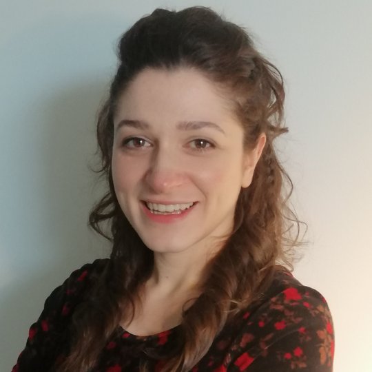 Porträtfoto von Mine Altinli, einer Nachwuchs-Forscherin mit lockigem Haar und schwarzer Bluse mit rotem Blumenmuster.