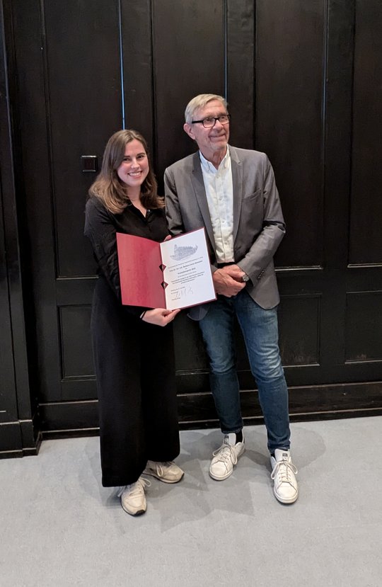 A board member of the Association of Friends of the Tropical Institute presents Barbara Honecker with a certificate at the award ceremony in the lecture theatre of the Bernhard Nocht Institute. In the background you can see a wall panelled in dark brown