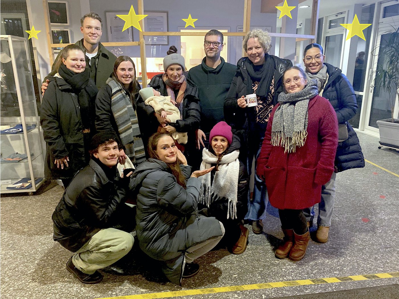 The picture shows the members of the Molecular Infection Immunology working group. The group is dressed in winter clothes and is standing in front of the reception of the Bernhard Nocht Institute.