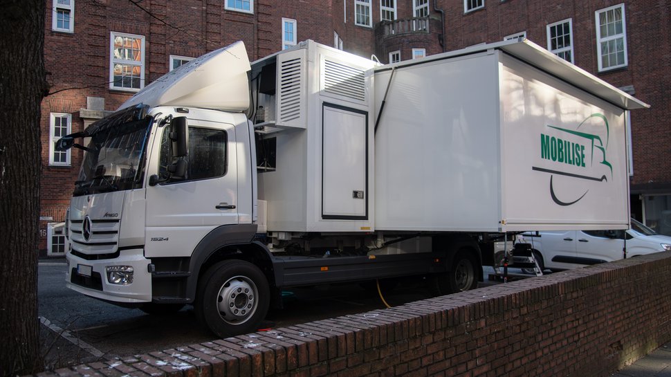 MOBILISE Wagen Vor einem roten Backsteingebäude steht ein weißer Lastwagen mit der Aufschrift MOBILISE