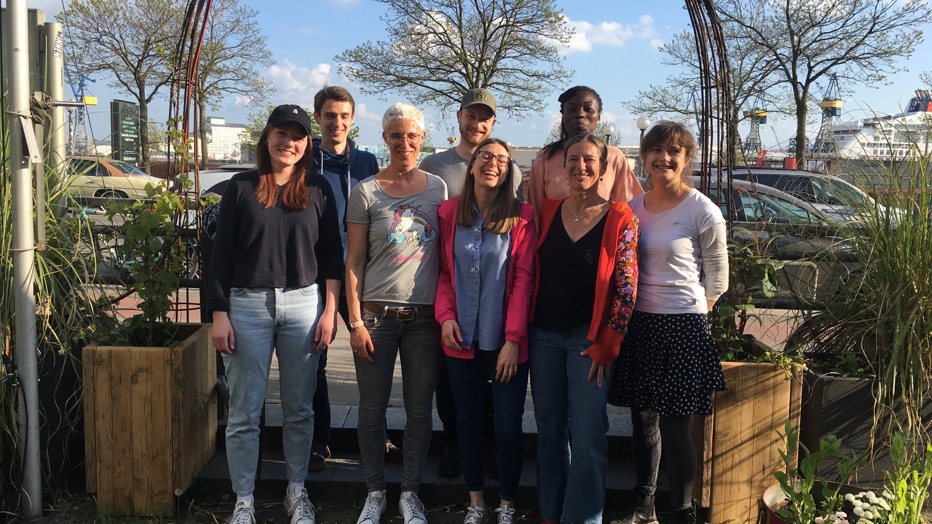 Gruppenbild der Ag Helminthen-Immunologie: Zu sehen sind 7 Personen die draußen vor einer großen Holztür als Gruppe gemeinsam stehen. Alle lachen in die Kamera.