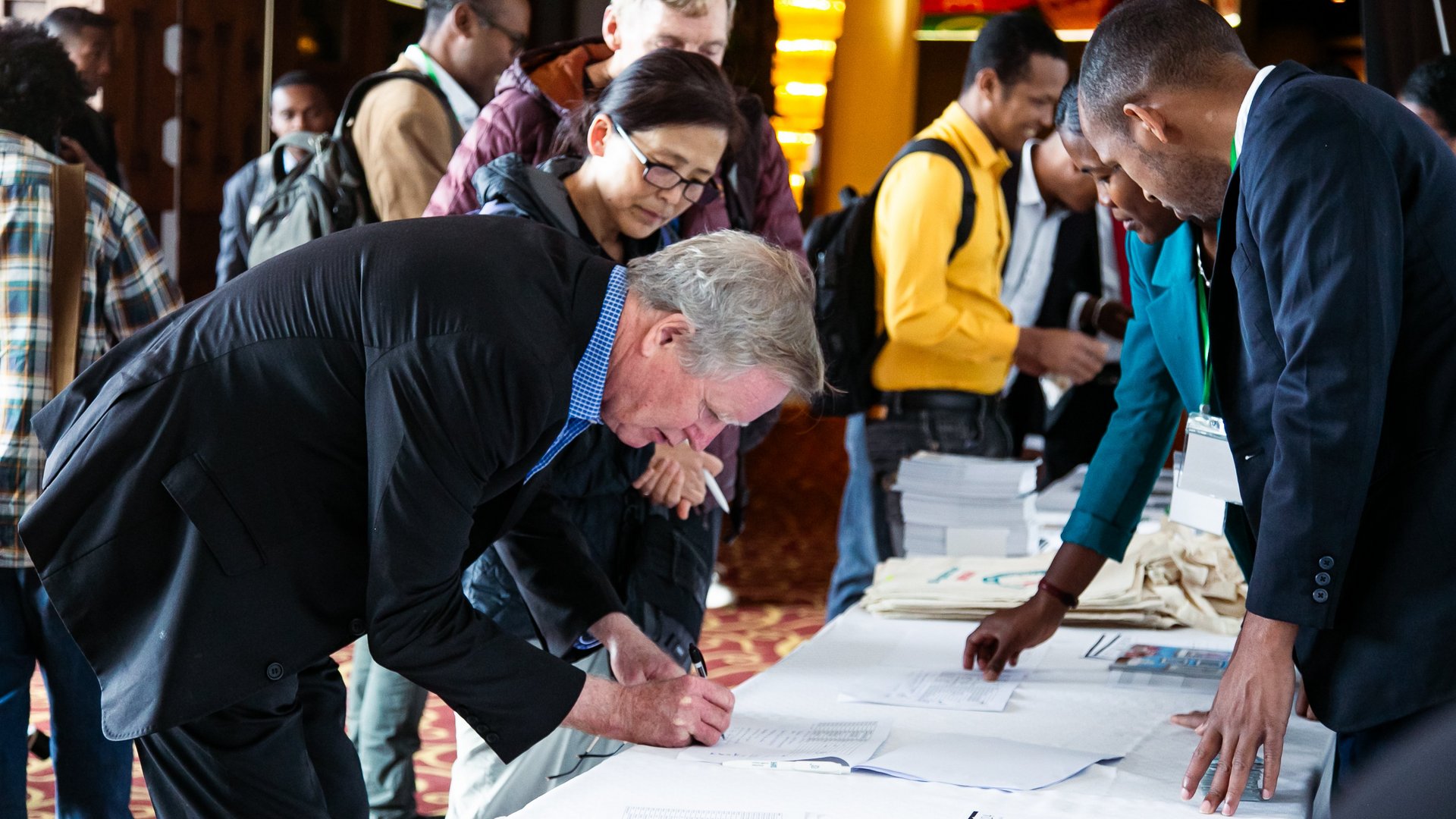CCSM conference attendees standing in line, holding documents and wearing event badges, some carrying tote bags with "DZIF" branding.