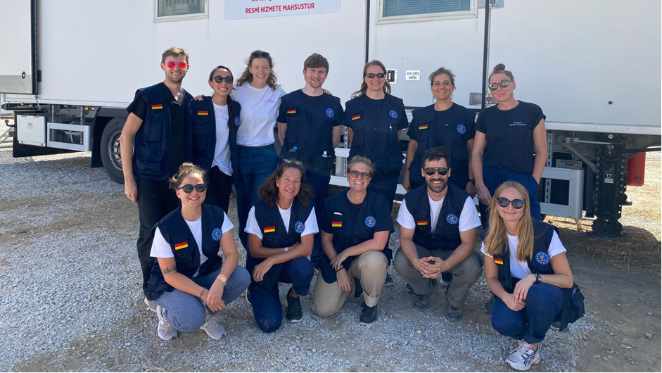 A picture of the twelve members of the EMLab Team in front of a white truck, all wearing blue EMLab shirts and vests, looking tired but very happy.