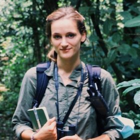 Dr. Elodie Freymann Dr. Elodie Freymann, a researcher, wearing a green shirt and backpack, holds a camera, ready to capture her surroundings during fieldwork.