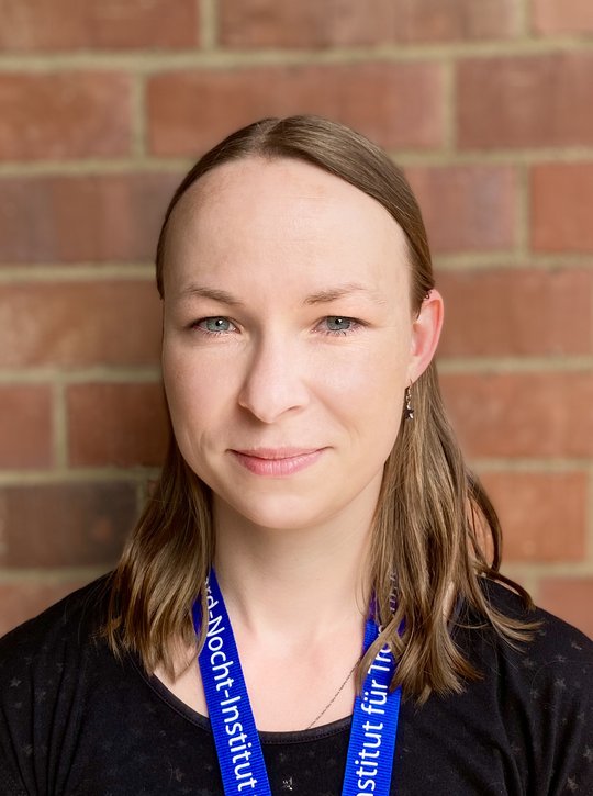 Dr. Maria Rosenthal Direktes Portrait von Maria Rosenthal vor einer Backsteinwand.