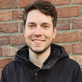 Dr Joachim Michael Matz: a researcher in front of a brick wall, wearing a hooded jacket, brown hair and a short chin beard.