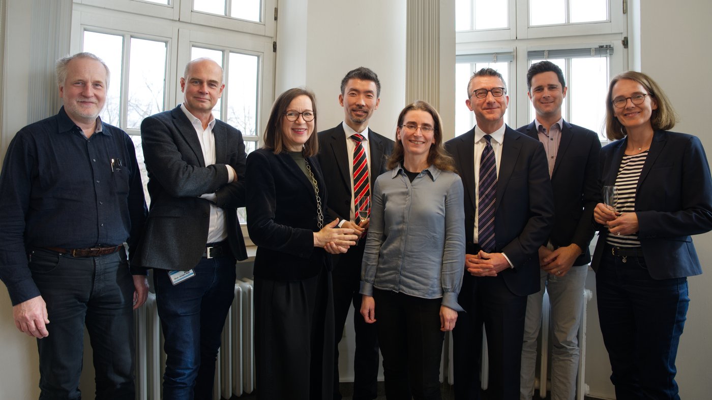 Das Foto zeigt eine Gruppe von Menschen mittleren Alters zum Teil mit Sektglas in der Hand, lächelnd.