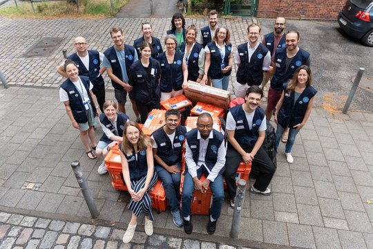 Gruppenfoto: Trainers und Trainees von BNITM und RKI auf orangen Kisten vorm BNITM sitzend