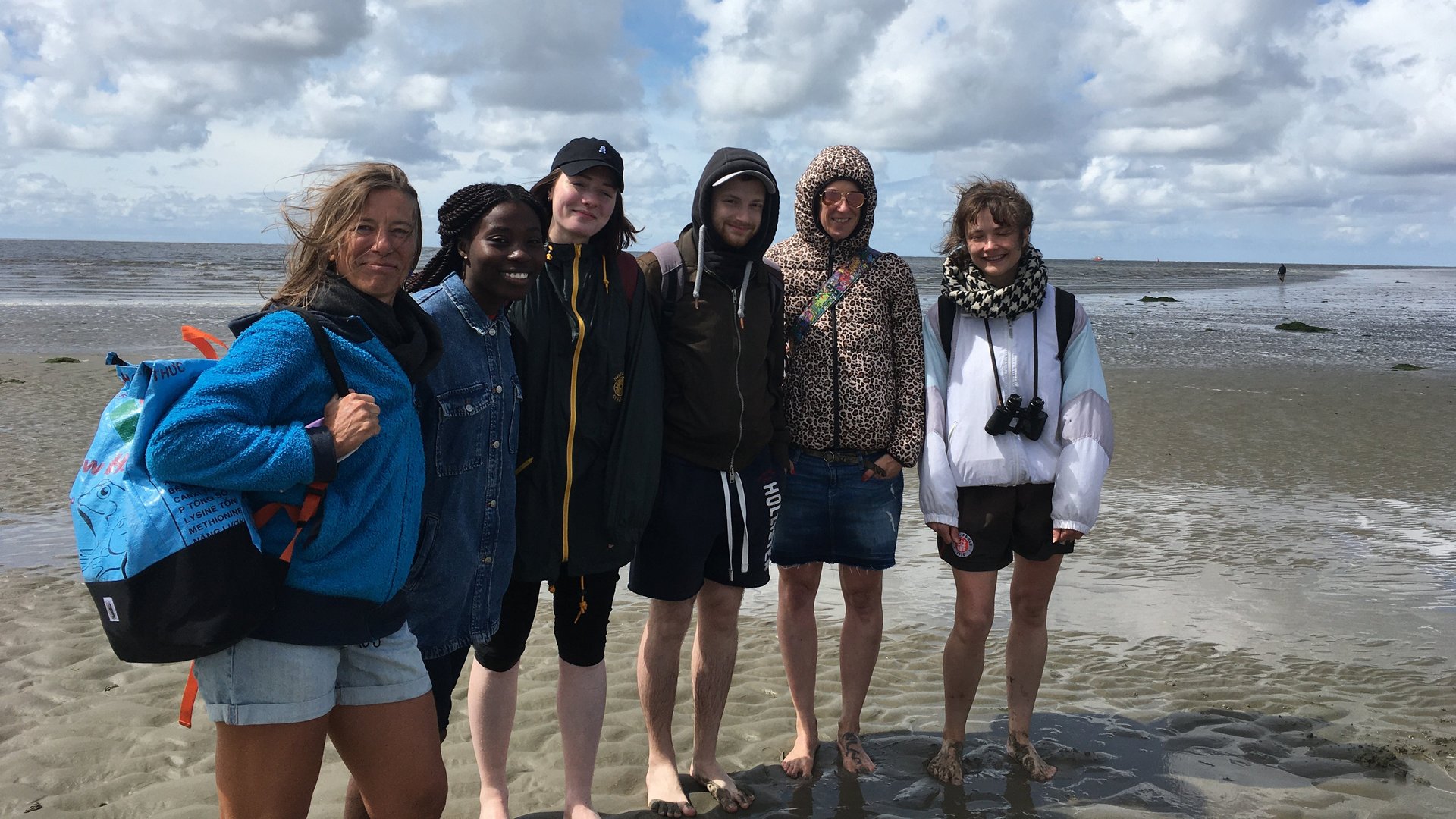 AG Helminthen-Immunologie im Watt bei Büsum: eine Gruppe von 6 Menschen stehen barfuß und mich hochgekrempelten Hosen im Watt und lachen in die Kamera. Im Hintergrund ist ein wolkiger Himmel zu sehen.AG Helminthen-Immunologie im Watt bei Büsum: eine Gruppe von 6 Menschen stehen barfuß und mich hochgekrempelten Hosen im Watt und lachen ausgelassen in die Kamera. Im Hintergrund ist ein wolkiger Himmel zu sehen.