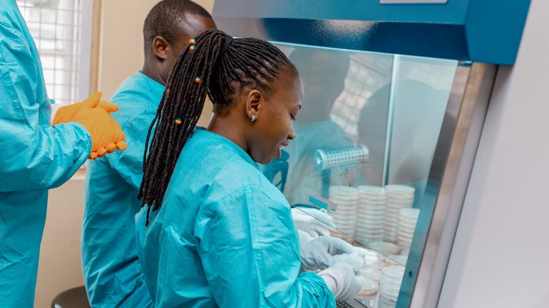 EAC Mobile Lab Train the Trainer Kursus Juni 2022, EAC Headquarter Arusha, Tansania Das Foto zeigt drei EAC lab experts in türkisen lab suits an der Bench arbeiten.