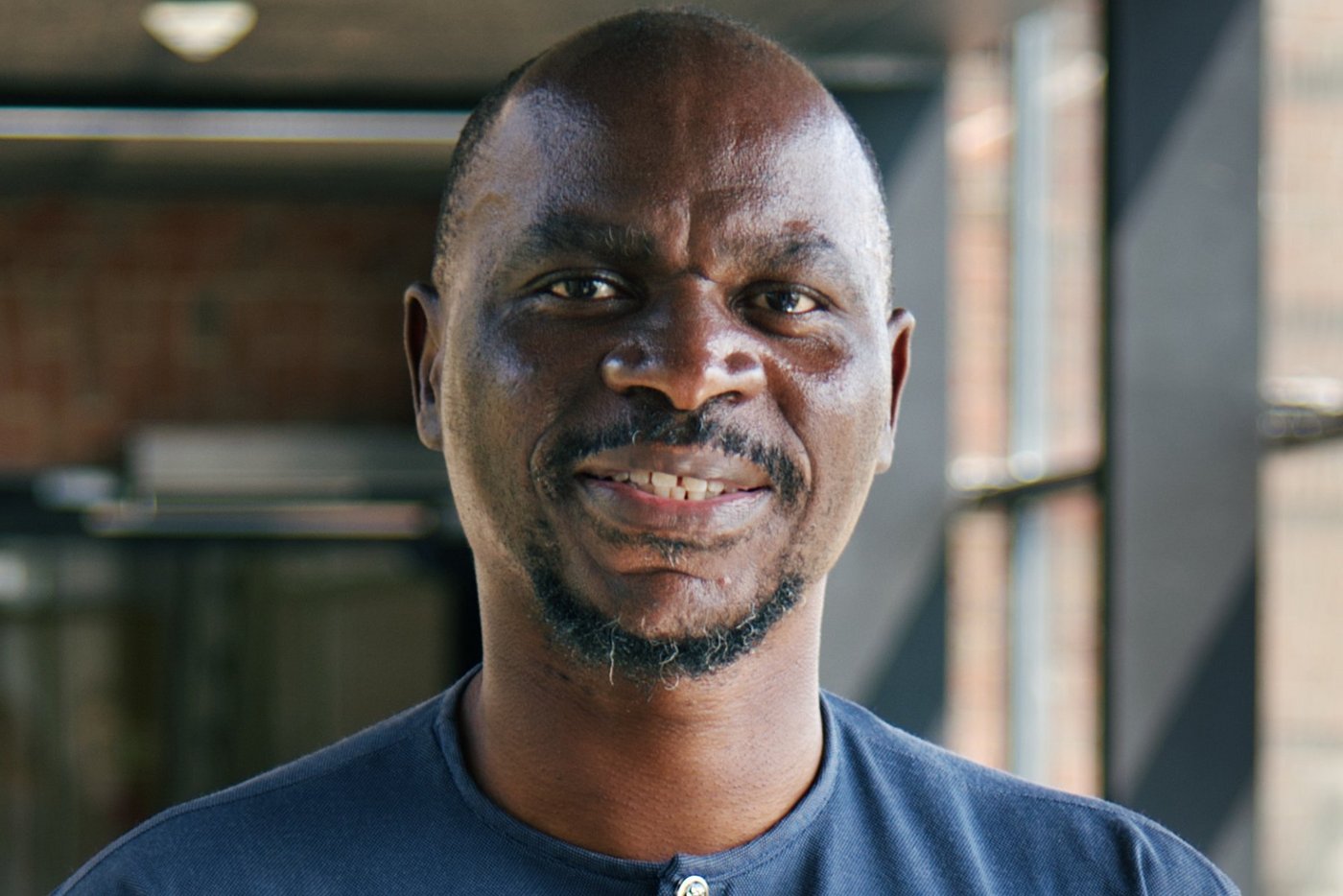 Portrait photo of Gabonese researcher Ghyslain Mombo-Ngoma: He is bald, has a short full beard and wears a dark blue African shirt and smiles at the camera.