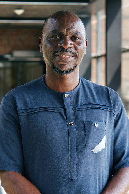 Prof. Dr. Ghyslain Mombo-Ngoma Porträt-Foto des gabonesischen Forschers Ghyslain Mombo-Ngoma: Er trägt Glatze, einen kurzen Vollbart und ein dunkelblaues afrikanisches Shirt und lächelt in die Kamera.