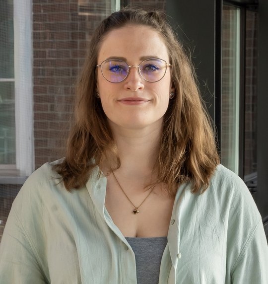 Portraitfoto der Nachwuchsforscherin Dr. Charlotte Hansen. Sie trägt schulterlange dunkle Haare, eine Brille, eine Halskette und ein hellgrünes Twinset. Sie blickt freundlich in die Kamera.