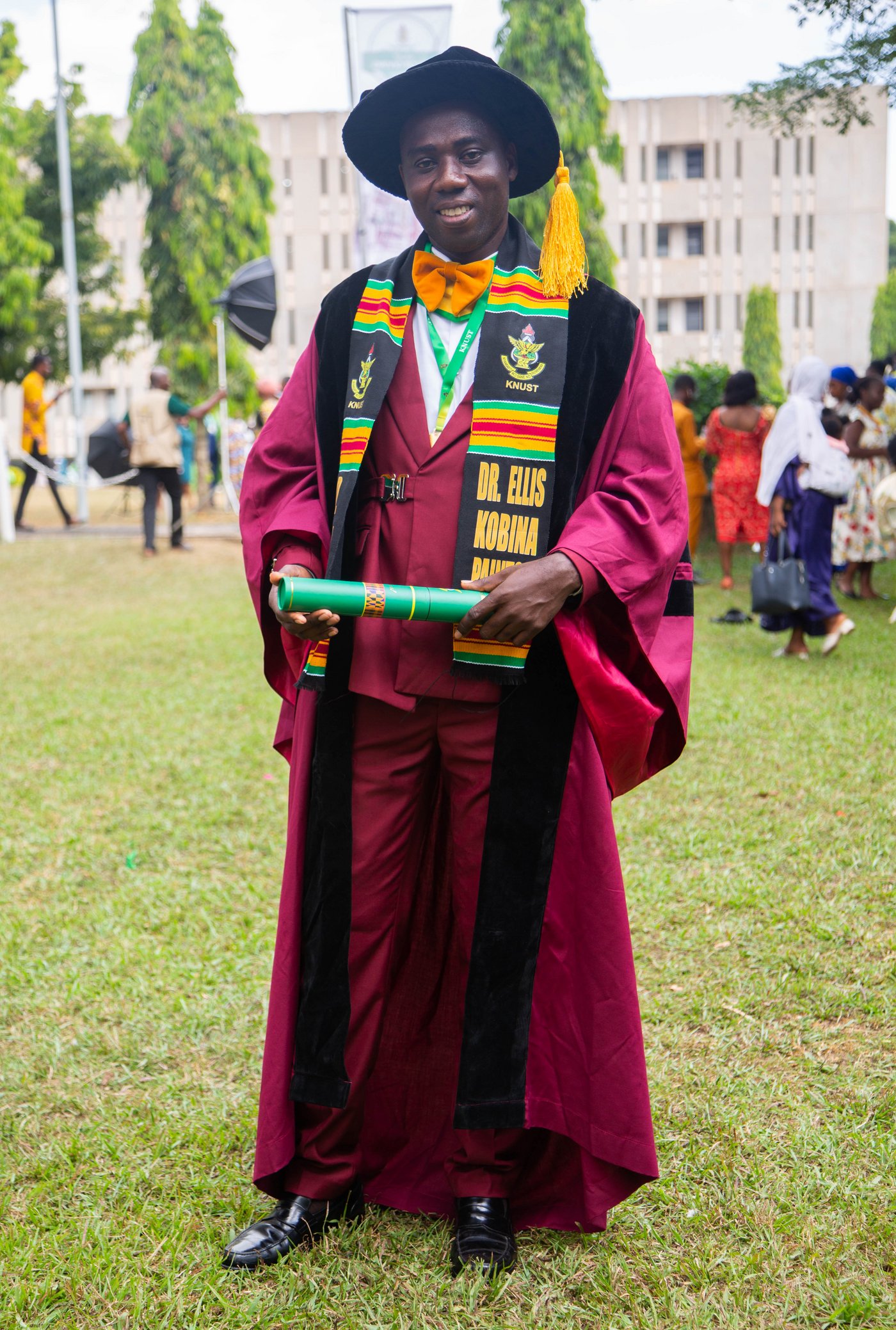 A man in a graduation robe and hat standing in the grass.