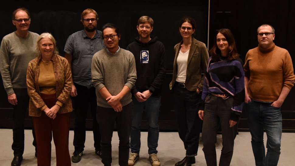 Das Foto zeigt zehn Forscherinnen und Forscher vor einer Leinwand im Hörsaal stehen.