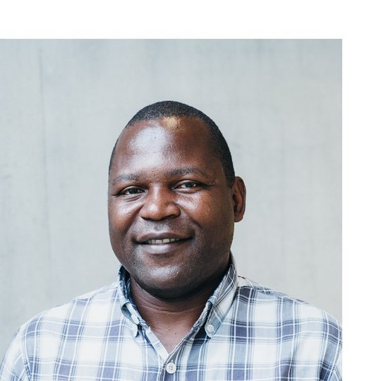 Portrait of a male Black person wearing a white and blue chequered shirt.