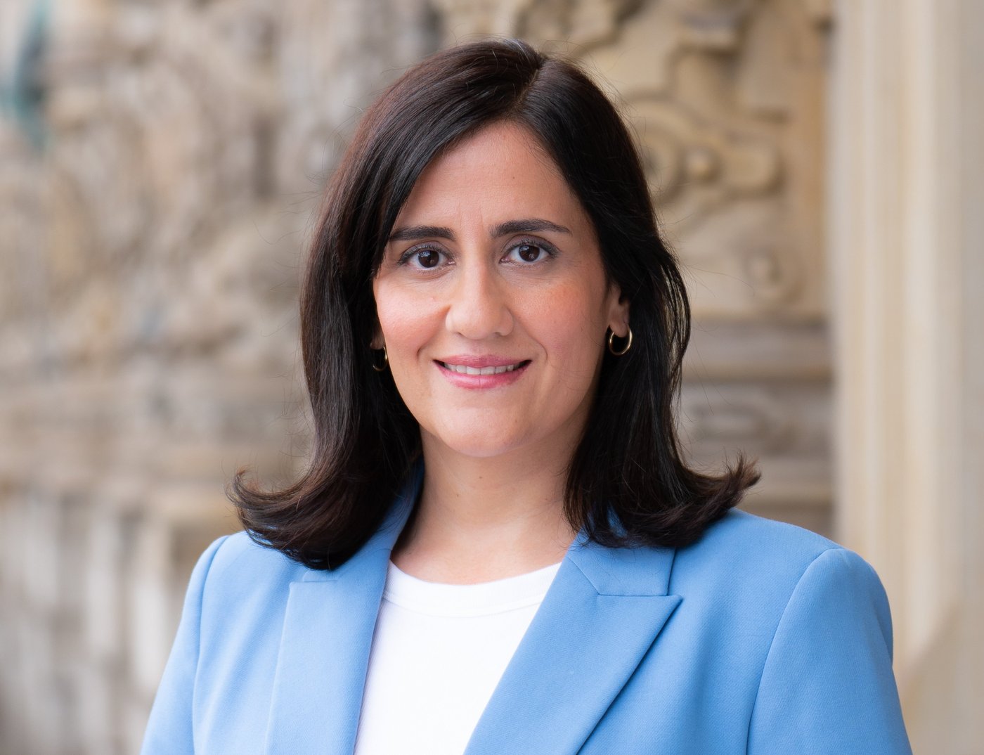 Hamburgs Wissenschaftssenatorin Maryam Blumenthal auf dem Balkon des Rathauses. Links rote und weiße Geranien, rechts eine Frau mit schulterlangen schwarzen Haaren, weißem Shirt unter hellblauem Blazer und freundlichem Blick.