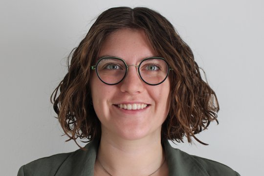 Eine junge Frau mit Brille schaut freundlich in die Kamera