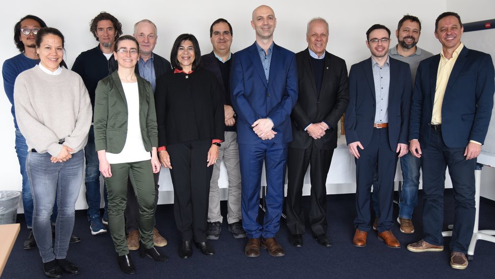 Gruppenfoto der Delegation von Fiocruz und der Gastgeber des BNITM. Zu sehen sind 12 Personen in zwei Reihen vor einer weißen Zimmerwand.