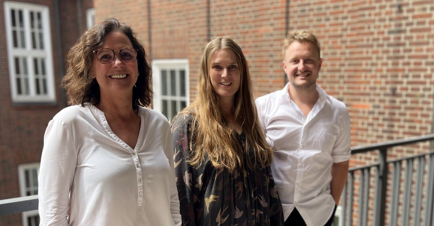 Bachmann laboratory group: a group of young researchers stands in front of the institute and laughs friendly into the camera.