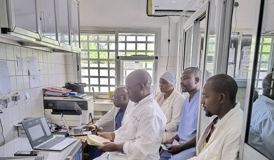 Laboratory team members sitting in the laboratory while attending the remote training on a laptop and taking notes.