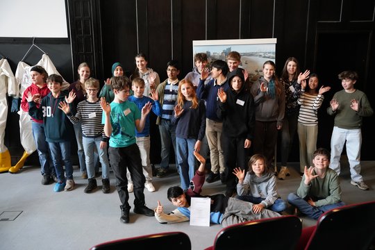 Gruppenfoto mit 25 Schüler:innen im Hörsaal des BNITN stehen vor einer dunklen Wand