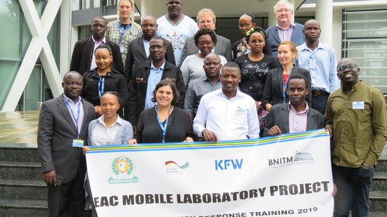Training Ebola 2019 Gruppe diverser Menschen, die ein Banner halten und freundlich Richtung Betrachter schauen.