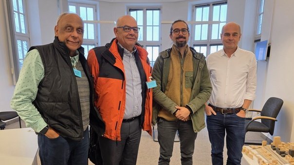 A group of four male international scientists posing for a group photo in the BNITM executive office, smiling and looking at the camera.