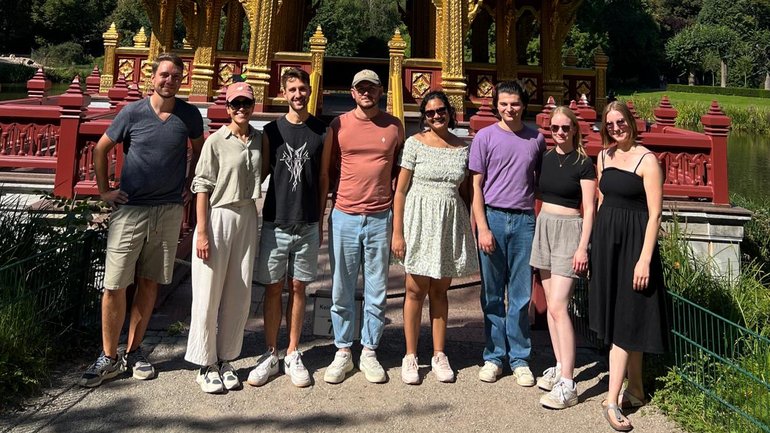 A team of eight scientists stands in front of a pagoda and smiles into the camera