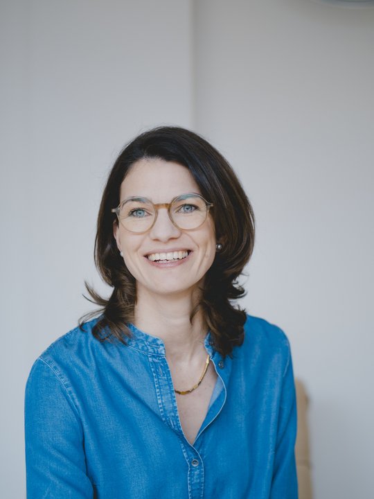 Portrait of a young, self-confidently smiling researcher with half-length brown hair and glasses