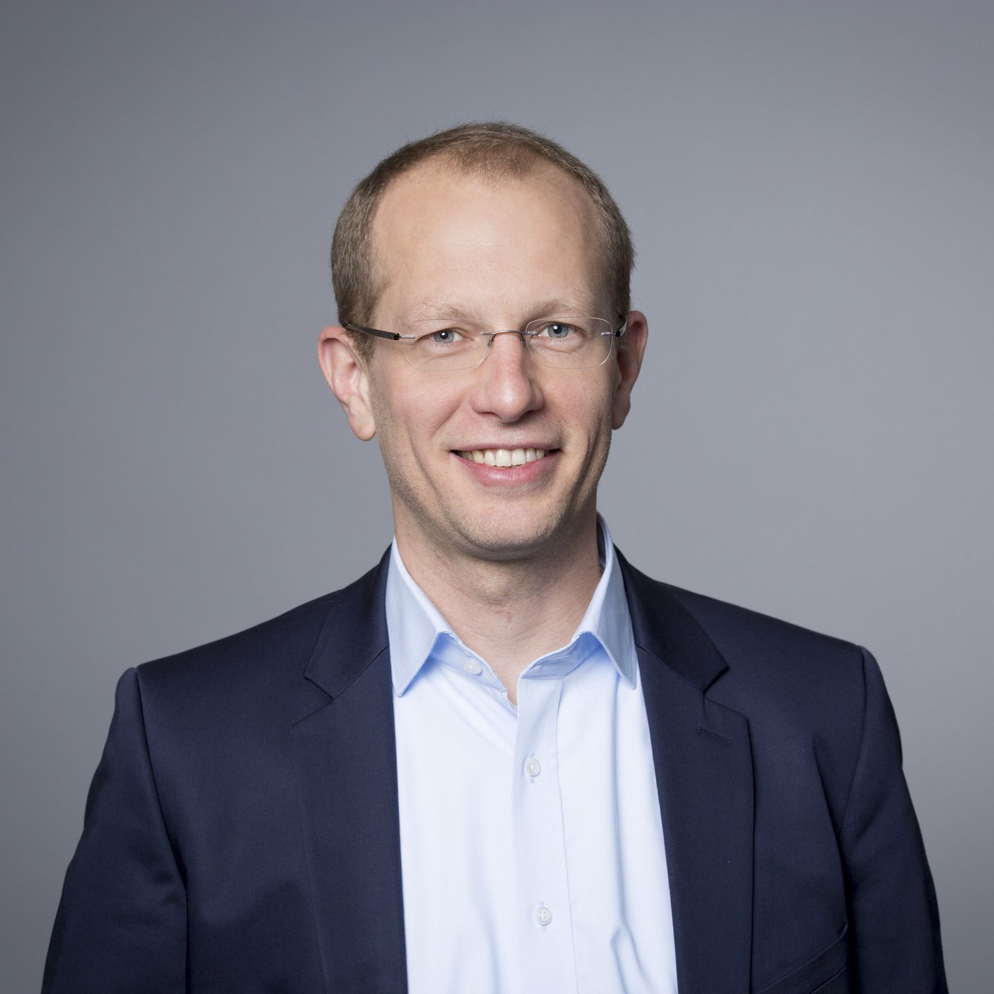 Prof. Michael Ramharter: a doctor with short blond hair and glasses, wearing a light blue shirt and a dark blue jacket.