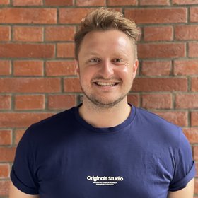 Yannick Daniel Höppner: ein Mann steht draußen vor einer Backsteinwand und lacht in die Kamera.