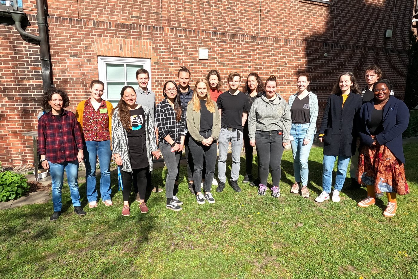 A group of trainees stand in front of a brick wall in the institute garden and smile.