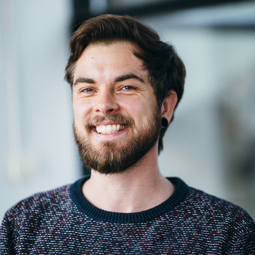 Erik Tove Zillmann portrait of a white male bearded person, wearing a blue-red-white sweater, smiling into the camera