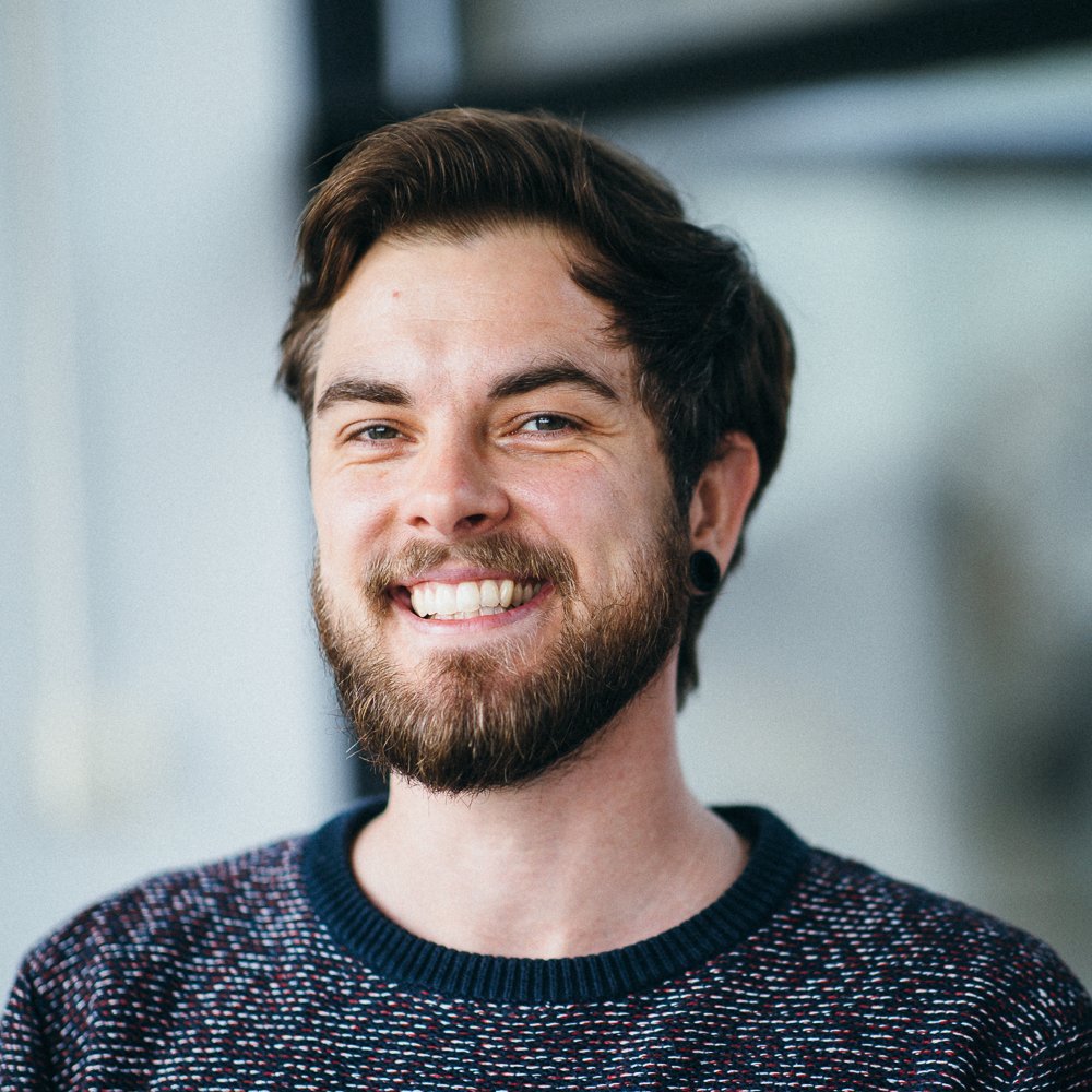 portrait of a white male bearded person, wearing a blue-red-white sweater, smiling into the camera