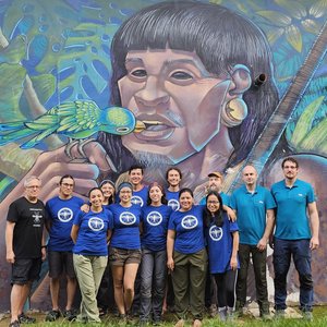 The photo shows a group of people in front of a larger-than-life colourful mural: an indigenous face from Peru, surrounded by jungle, with a parrot flying into its mouth. In keeping with the One Health concept.