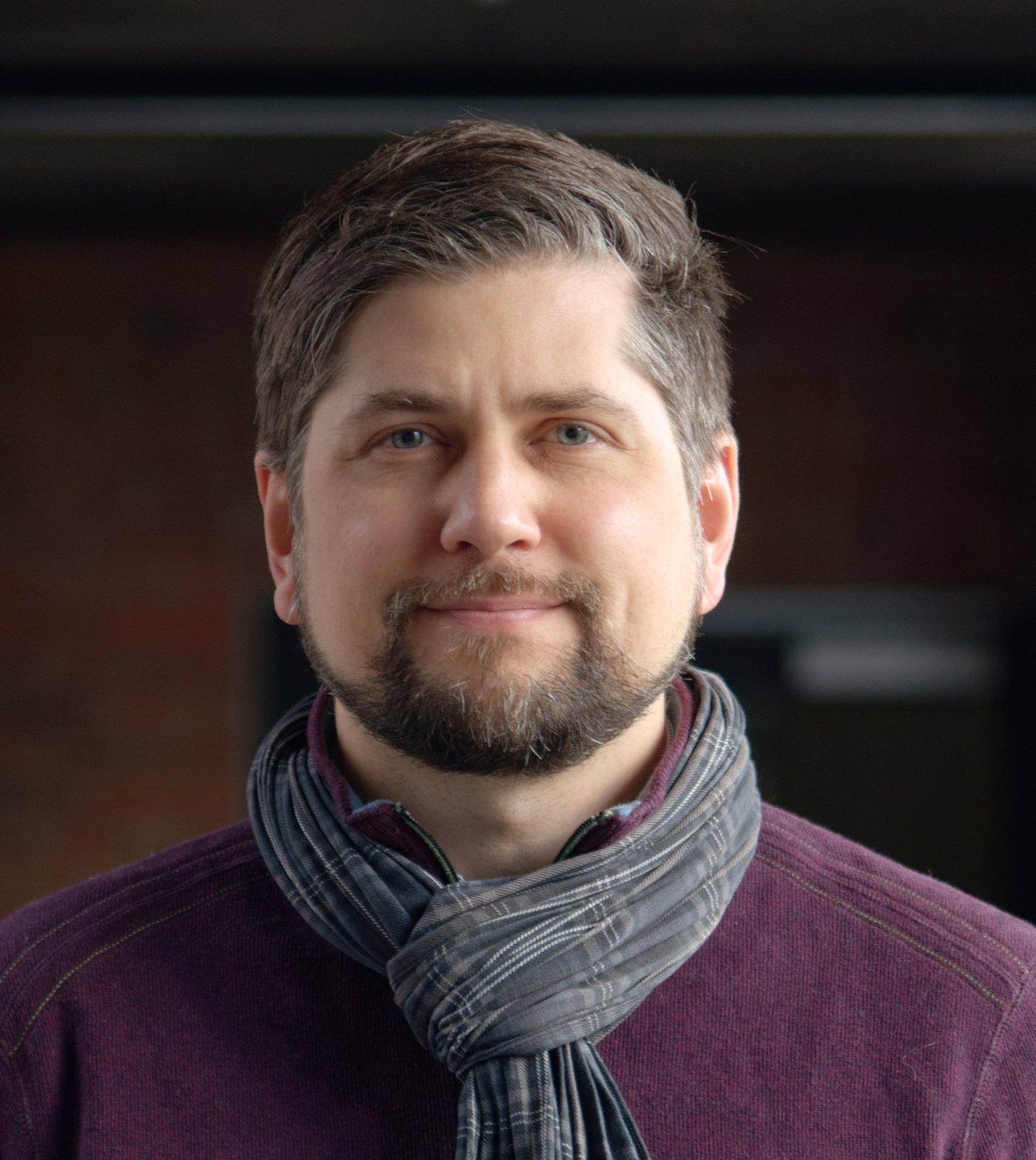 Dr. Johannes Mischlinger Dr. Johannes Mischlinger: ein Gruppenleiter, der kurzes, nach hinten gegeltes braun-graues Haar, einen leichten Bart, einen Schal und ein lila farbendes Oberteil trägt.