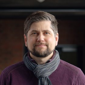 Dr Johannes Mischlinger: a group leader wearing short, slicked-back brown-grey hair, a light beard, a scarf and a purple-coloured top.