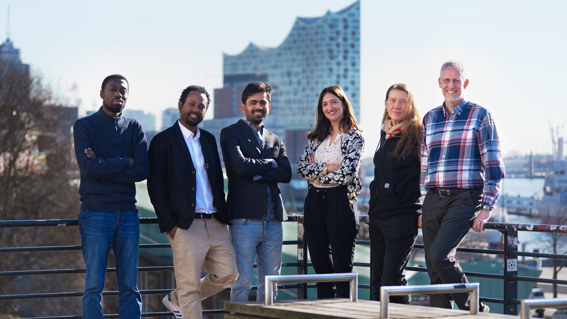 An ethnically mixed group of scientists looking friendly into the camera in front of a sunlit harbour