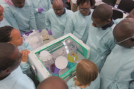 Training an der Glove box Das Bild zeigt verschiedene Forscher, die einer weiteren bei Laborarbeiten zusehen