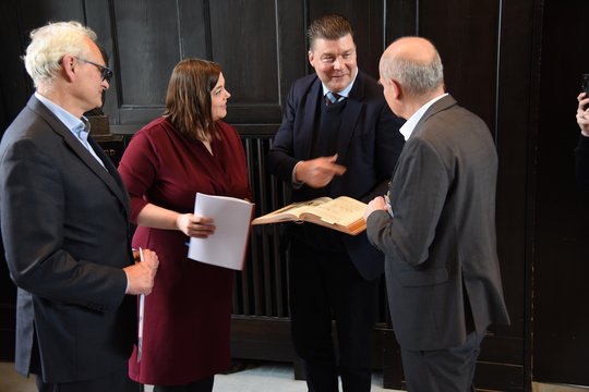 Das Bild zeigt v.l.n.r. Martin Görge, Katharina Fegebank, Andreas Dressel und Jürgen May. Sie beugen sich über ein historisches Buch über das BNITM von 1914.