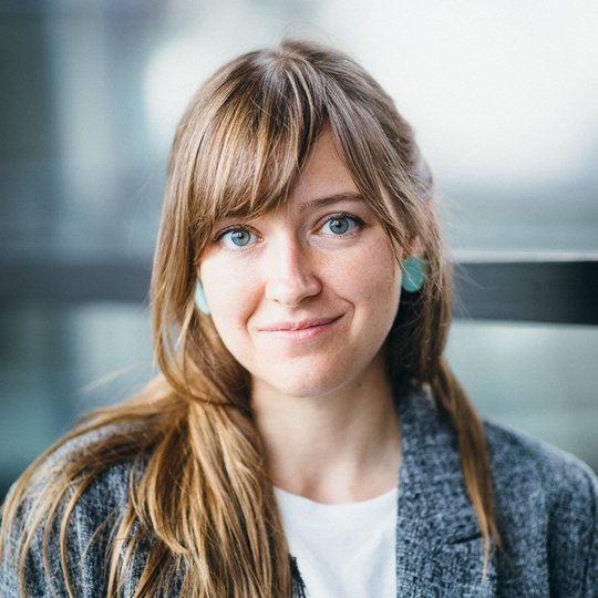 Portrait of a white female person with long brown hair, wearing a grey suit and a white shirt.